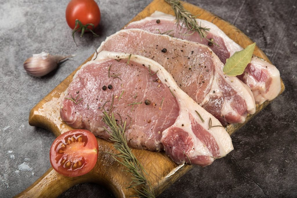 A fresh arrangement of raw pork chops seasoned with herbs and spices, ready for cooking.